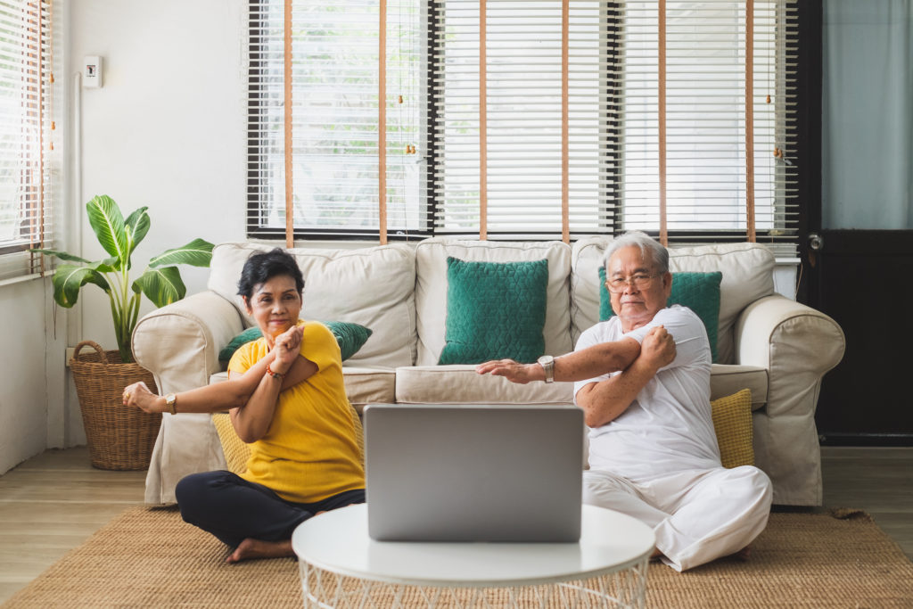 An elderly man and a middle aged woman doing yoga at home