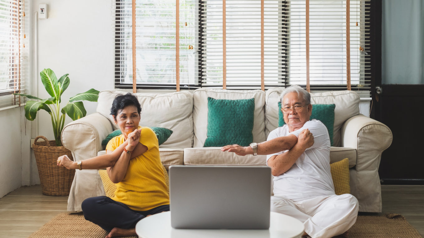 An elderly man and a middle aged woman doing yoga at home