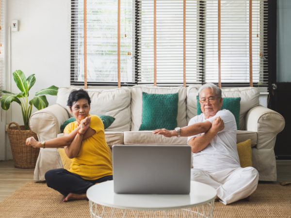 An elderly man and a middle aged woman doing yoga at home