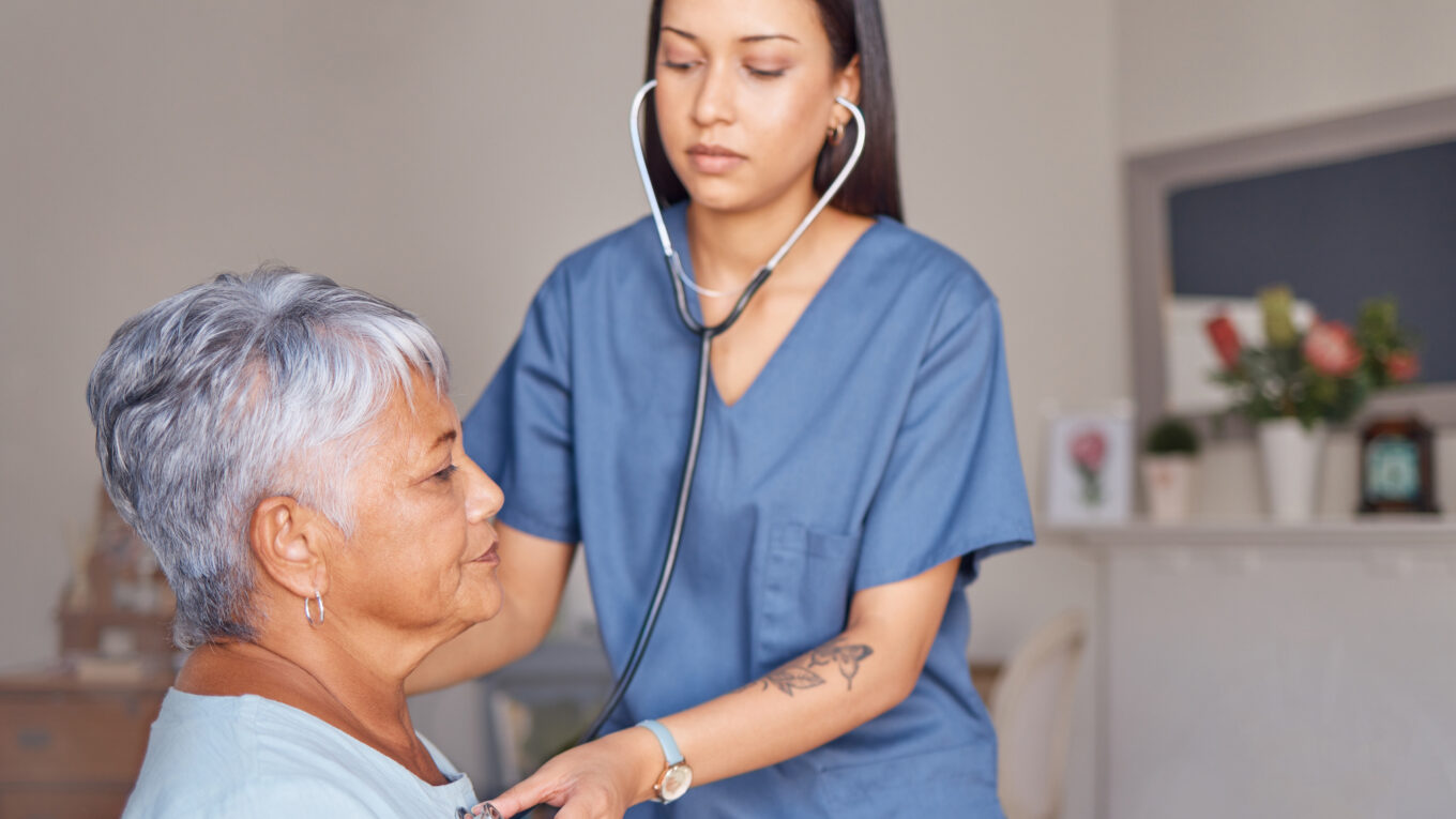 Nurse with a stethoscope listening to heartbeat of an elderly patient during a health consultation.