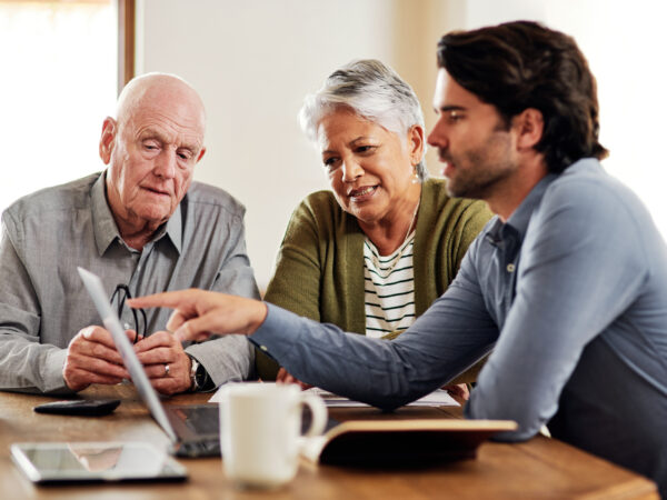 Two older people look at a laptop, and a younger man is pointing at the screen