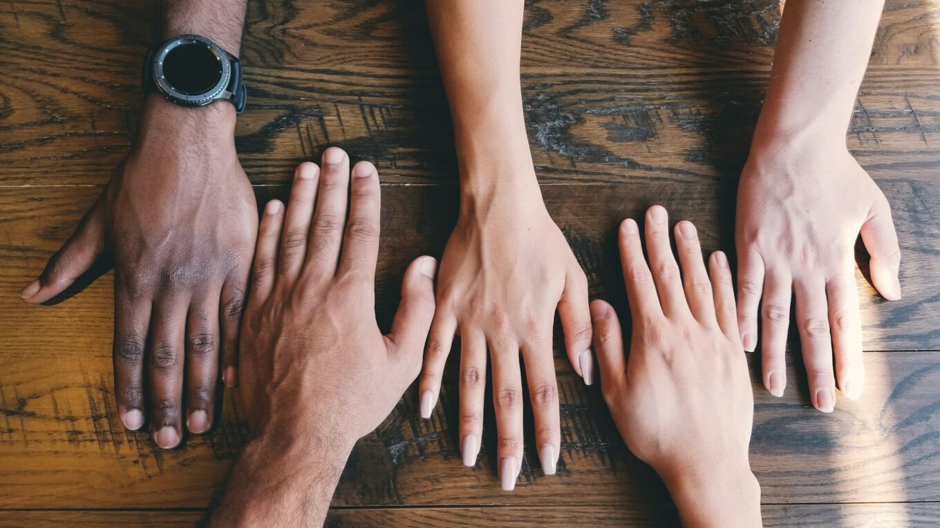 Hands of people of different ages, genders and ethnicities on a table