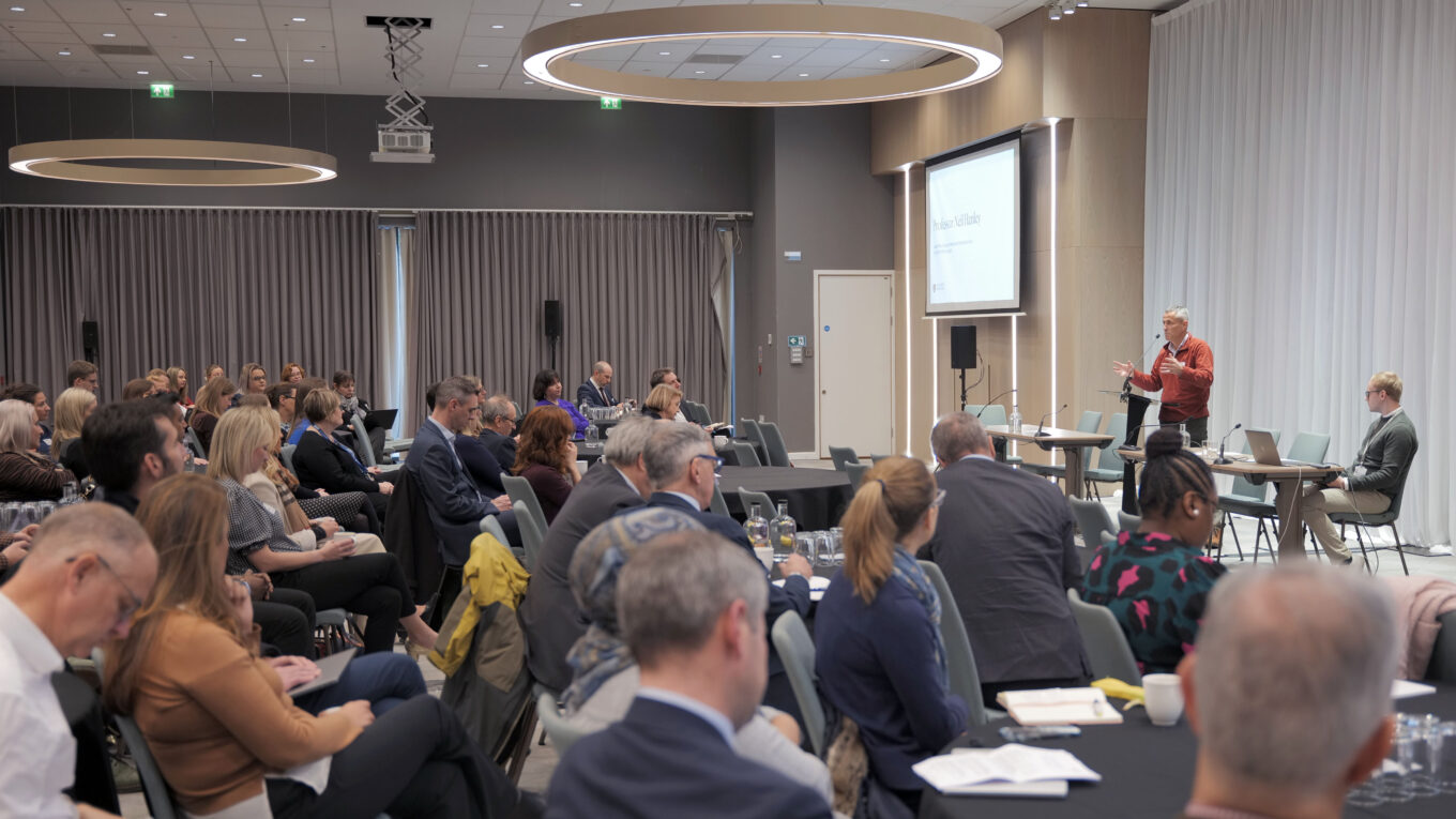 Full room of attendees at the UoB and NIHR Research Showcase, with Neil Hanley speaking on stage