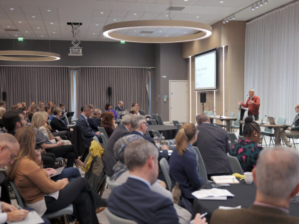 Full room of attendees at the UoB and NIHR Research Showcase, with Neil Hanley speaking on stage